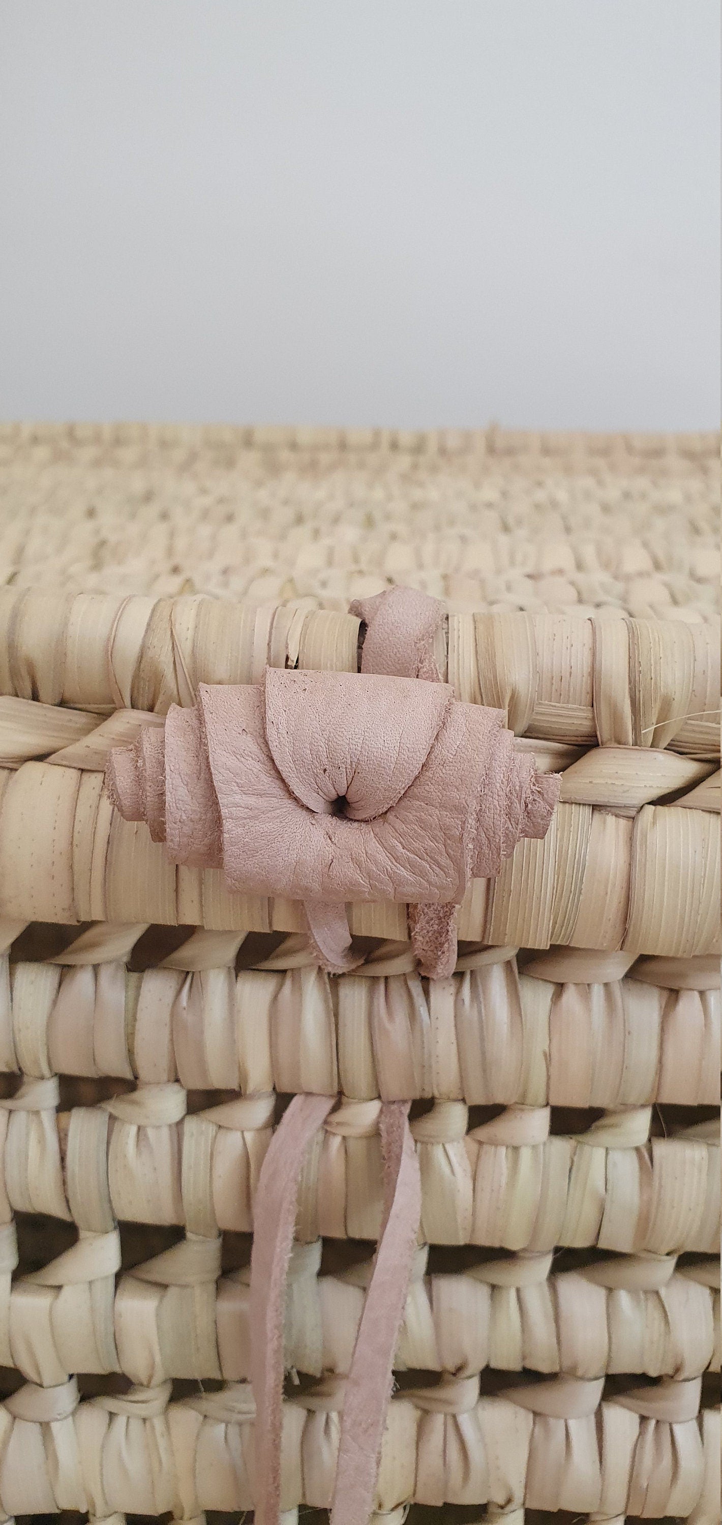 Cette malle en osier avec une anse en cuir offre un rangement élégant et s'intègre harmonieusement dans n'importe quelle pièce