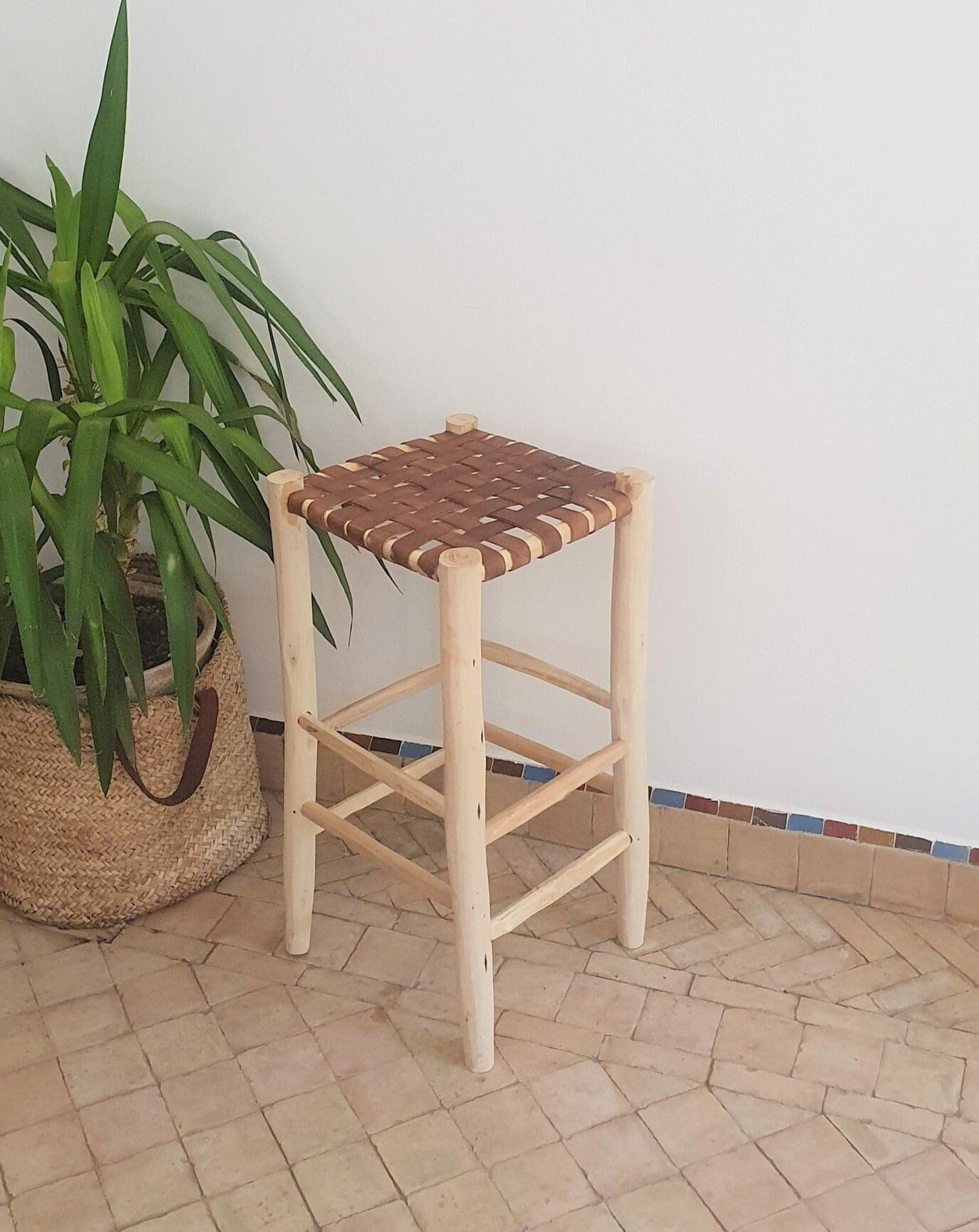 Tabouret de bar design marocain en bois de laurier avec une élégante assise en cuir de couleur camel.