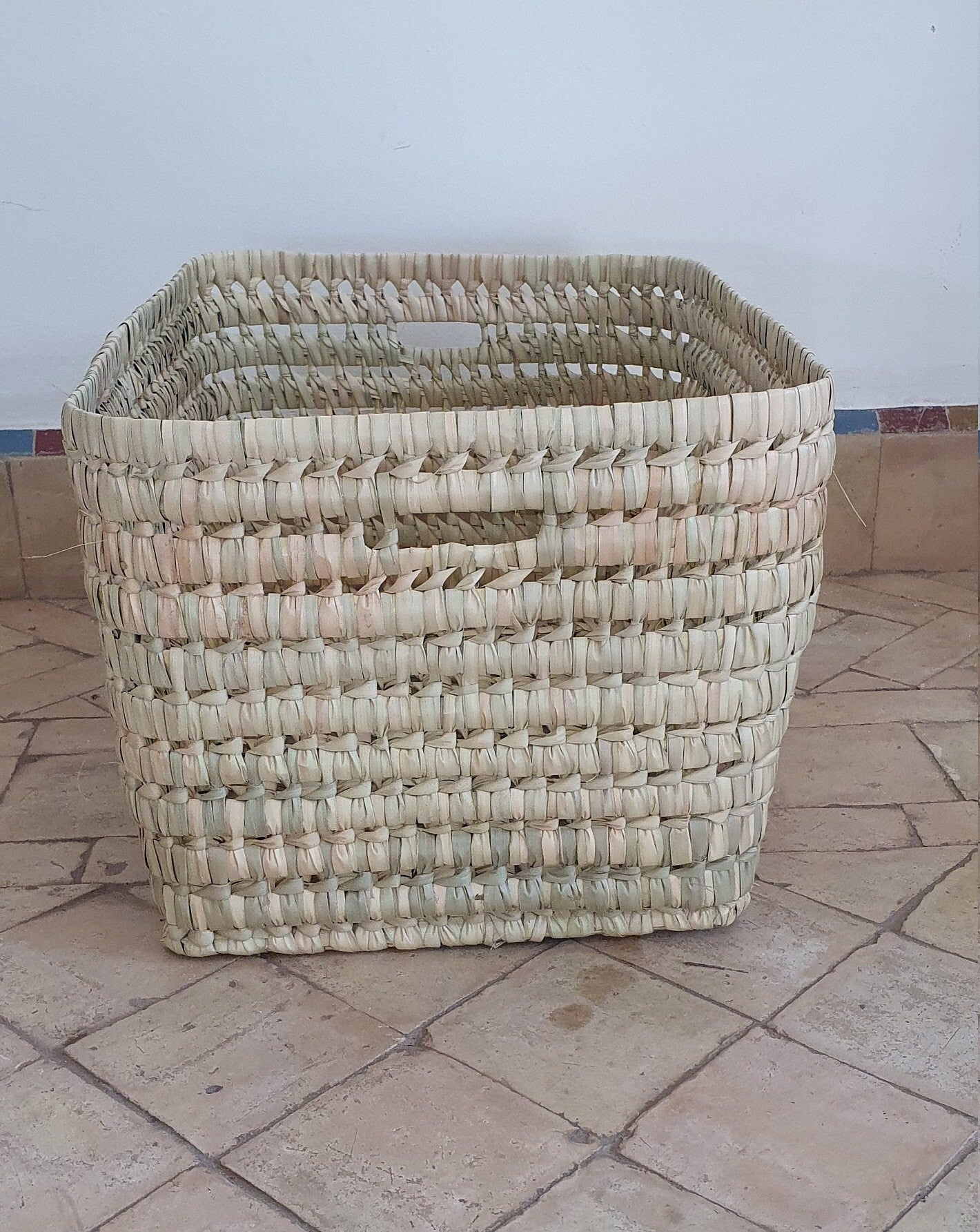 Ce panier en feuilles de palmier et osier, un mélange de style et de durabilité, est un accessoire incontournable pour la maison.