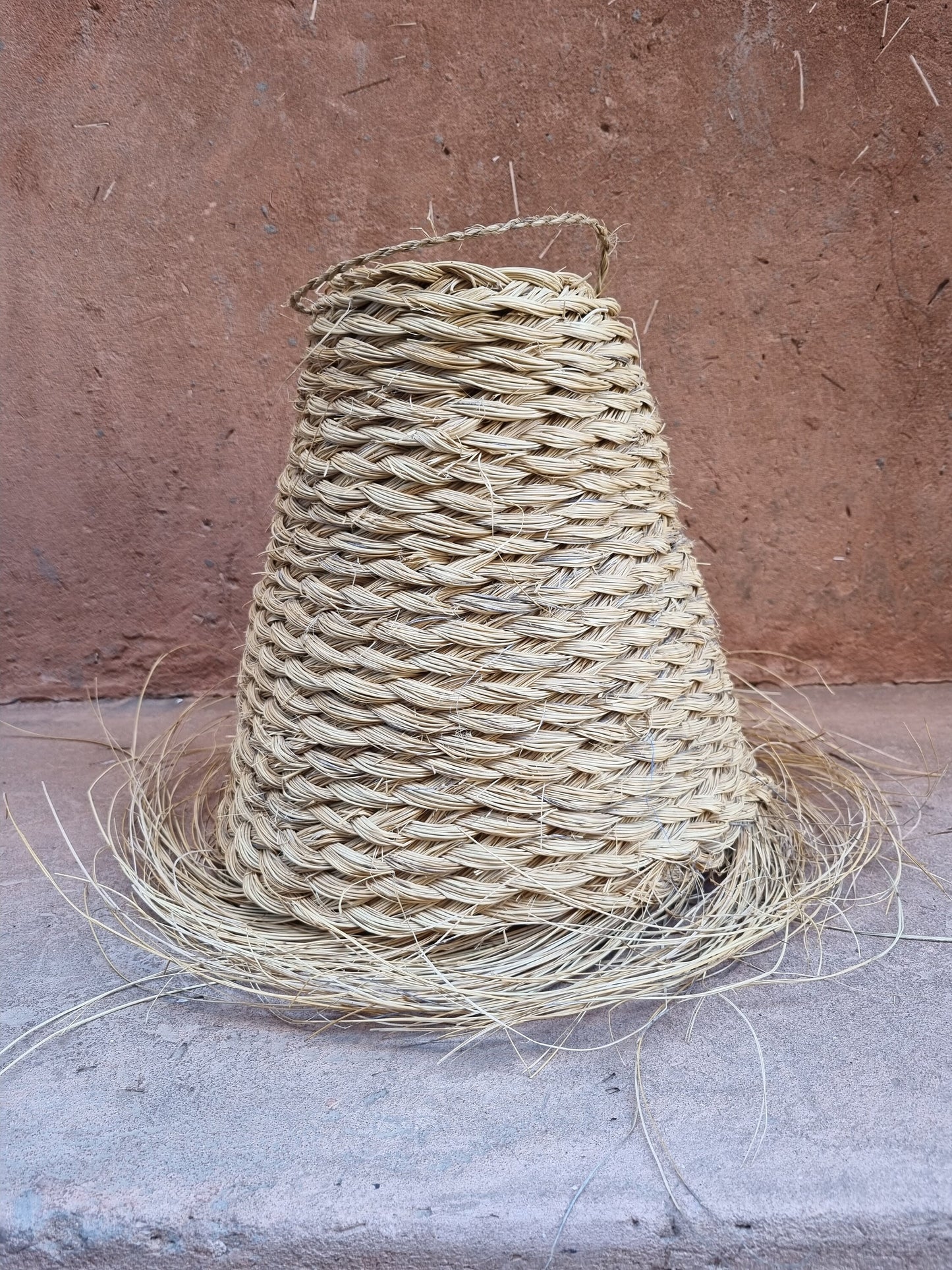 Handwoven doum fiber suspension lamp with a conical design.