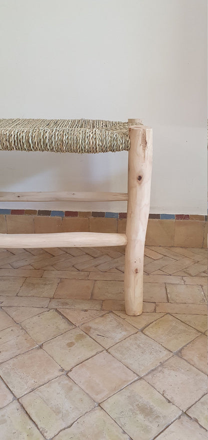 A side view of a rustic wooden bench featuring intricate natural weaving on the seat and backrest.