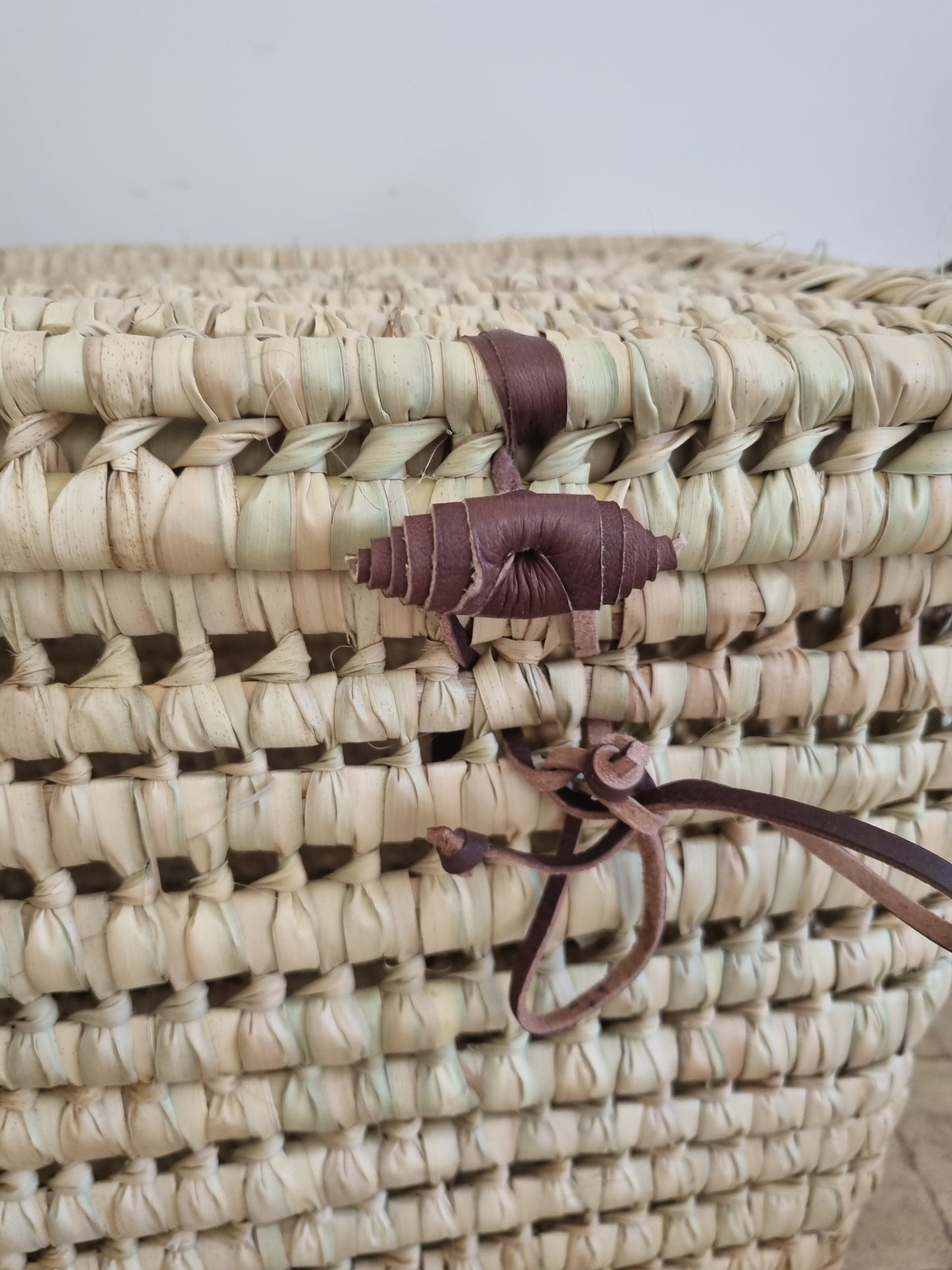 Close-up of leather handles on wicker storage box